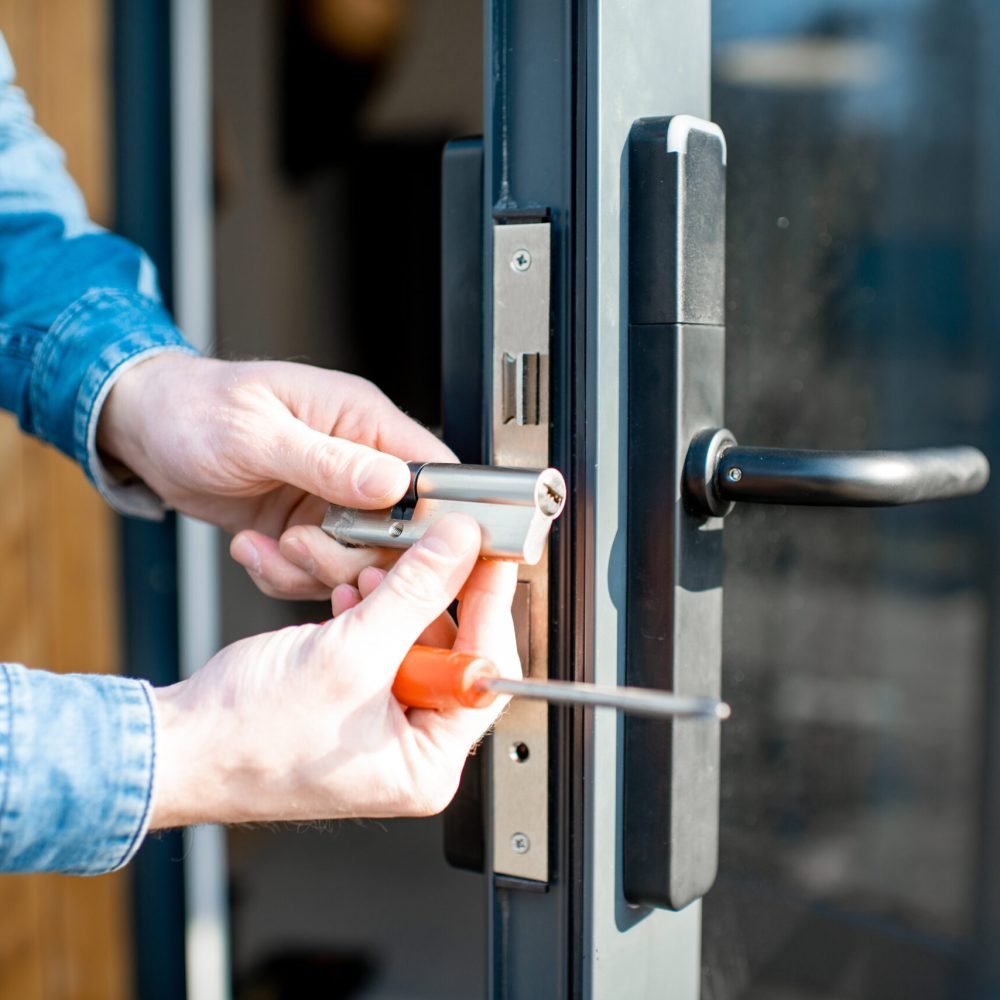 Man changing core of a door lock of the entrance glass door, close-up view with no face